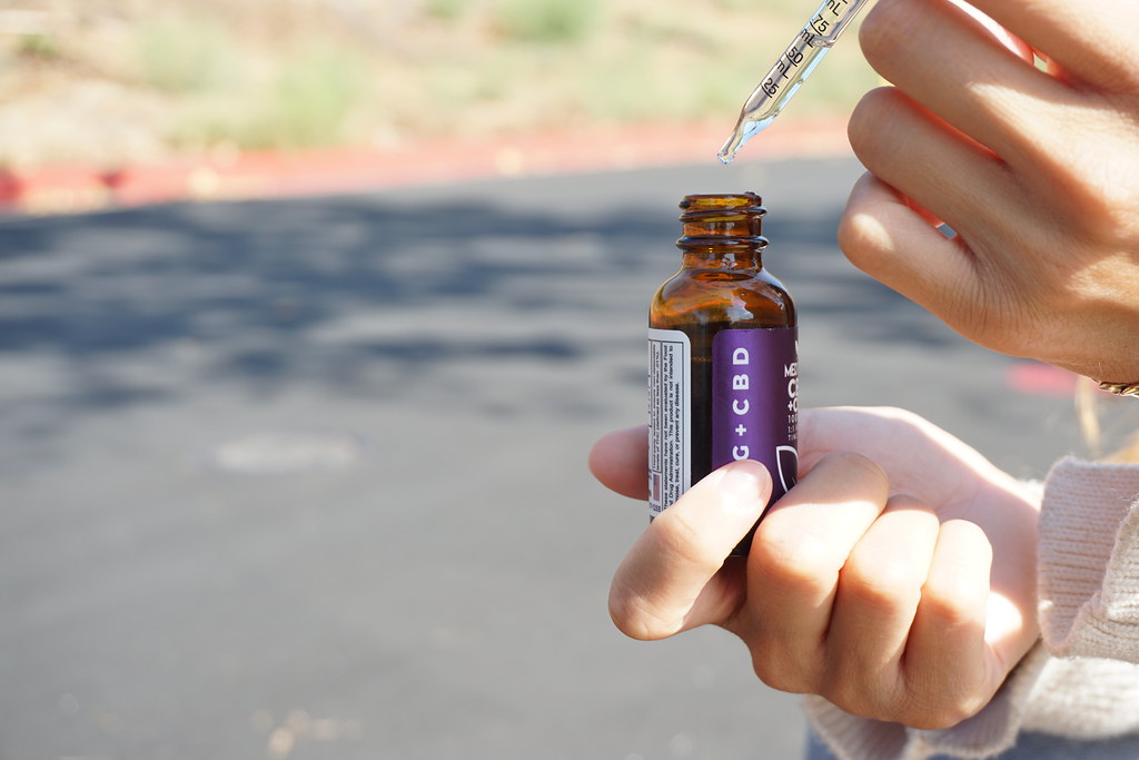 Hand holding a CBD oil bottle and dropper outdoors